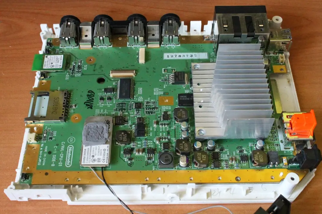 A picture of a Wii motherboard, surrounded by the white plastic, on a wooden background.